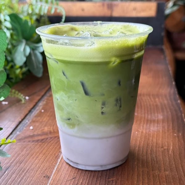 Iced matcha latte with a distinct green top layer and white bottom layer, on a wooden table.