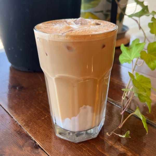 Iced latte with foam and ice on a wooden table next to a green plant.