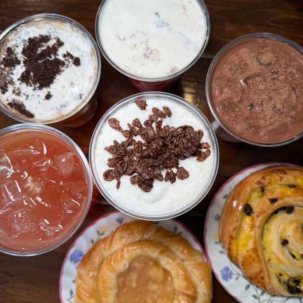Overhead view of various KOHI Coffee drinks and pastries on a wooden table.
