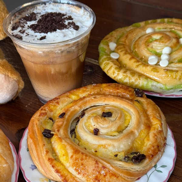 Iced coffee with whipped cream and cookie crumbles, alongside two spiral pastries on plates.