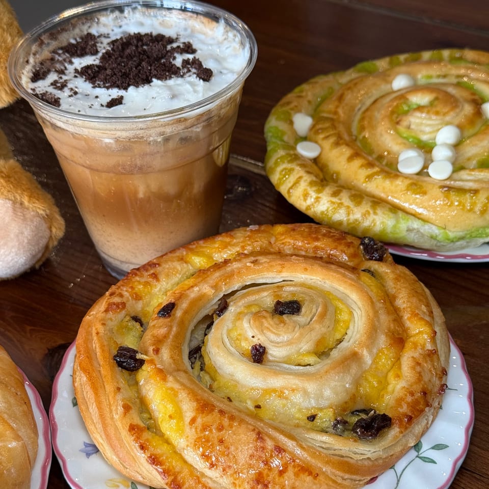 Iced coffee with whipped cream and cookie crumbles, alongside two spiral pastries on plates.