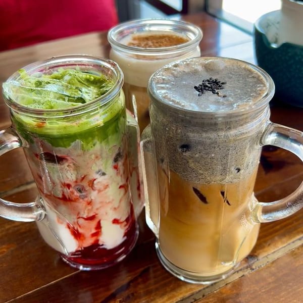 Three colorful iced drinks in glass mugs on a wooden table at KOHI Coffee.