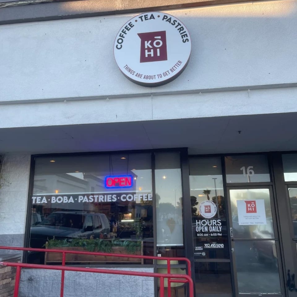 Exterior of KOHI Coffee shop with a circular sign, an "OPEN" neon sign, and hours of operation.