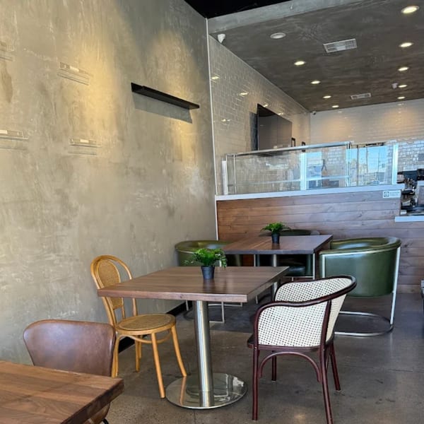 Interior of KOHI Coffee with wooden tables, various chairs, and a counter with a clear barrier.