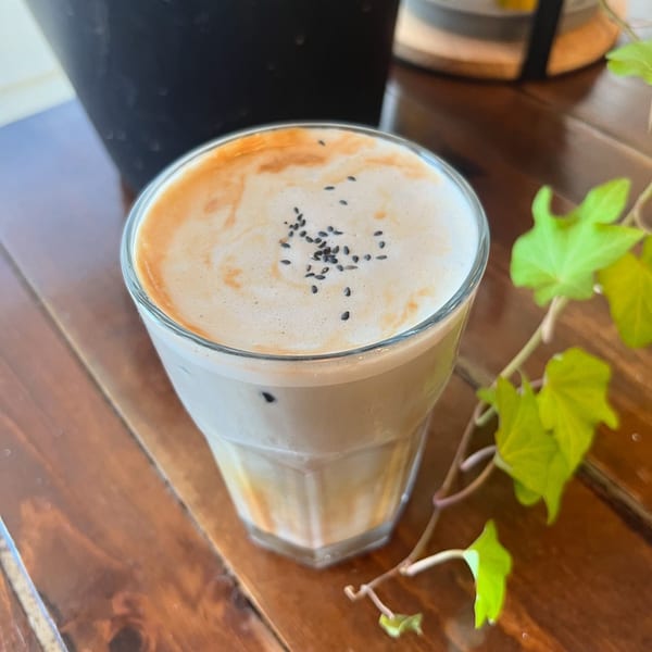 Iced latte with foam and black sesame seeds on a wooden table with green leaves.