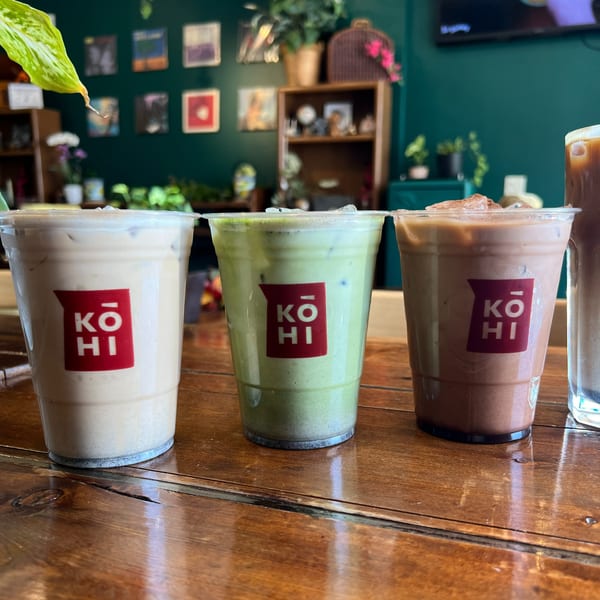 Three iced KOHI Coffee drinks, including matcha and chocolate, on a wooden table.