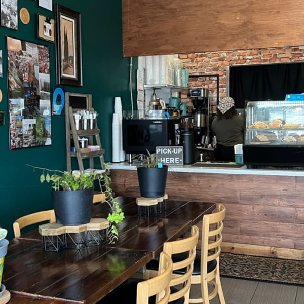 Interior of KOHI Coffee with a long wooden table, green walls, and a barista behind the counter.
