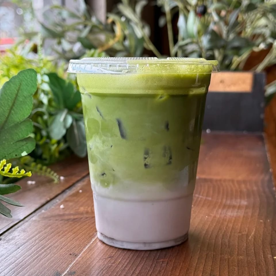 Iced matcha latte with a distinct green top layer and white bottom layer, on a wooden table.