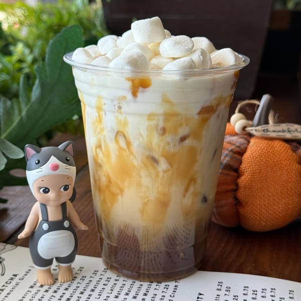A KOHI Coffee iced caramel drink with marshmallows, a cat figurine, and a pumpkin decoration.