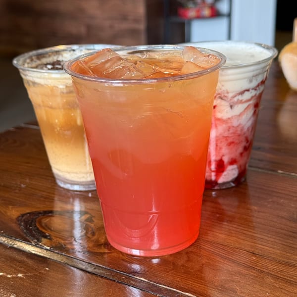 Three iced drinks from KOHI Coffee, including a vibrant red and orange iced tea, on a wooden table.