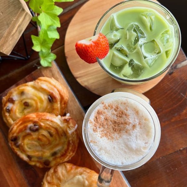 Overhead view of an iced matcha latte, a hot latte, and two pastries on a wooden table.