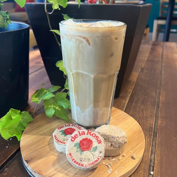 Iced coffee with three Mazapan candies on a wooden board, with green ivy and dark planters.
