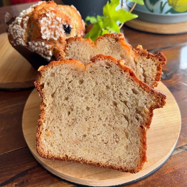 Slices of freshly baked bread and a blueberry muffin with sugar crystals on a wooden board.