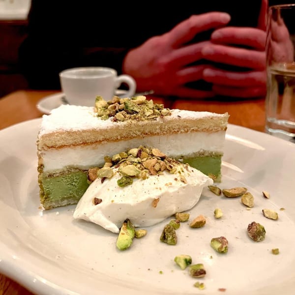 Slice of pistachio cake with whipped cream and chopped pistachios on a white plate at KOHI Coffee.