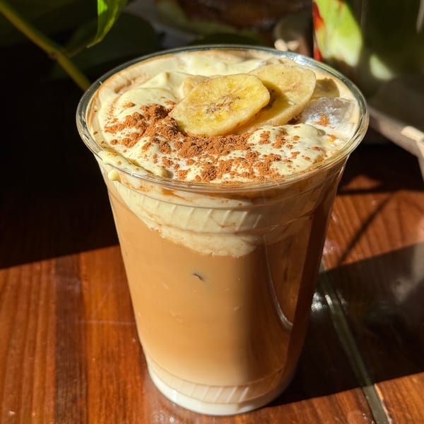 Iced coffee with whipped cream, banana slices, and cocoa powder on a wooden table.