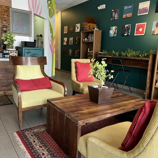 Cozy cafe interior with vintage chairs, a wooden coffee table, and record album art on a green wall.