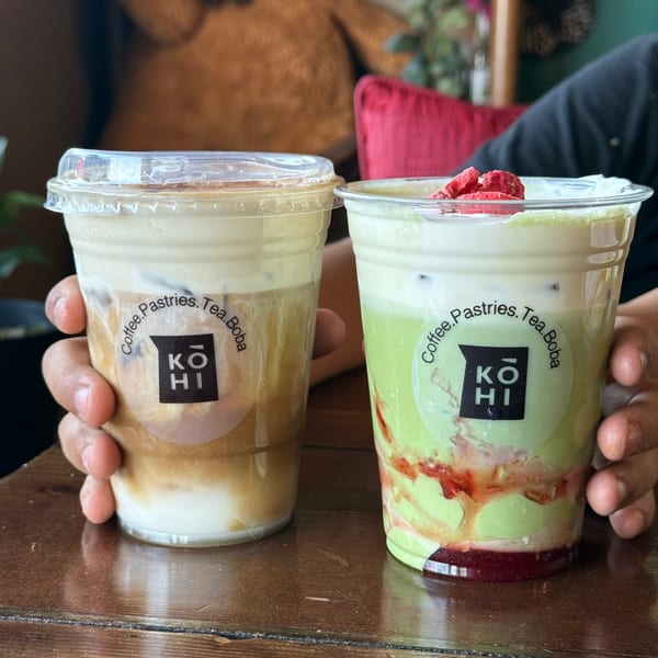 Two hands holding two iced drinks from KOHI Coffee, one coffee and one green tea with strawberry.