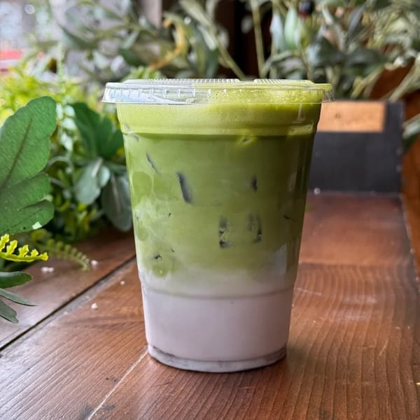 Iced matcha latte with a distinct green top layer and white bottom layer, on a wooden table.