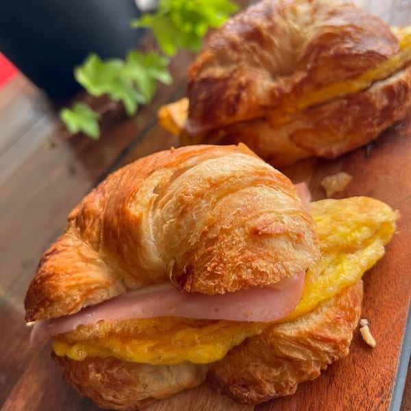 Two golden croissants filled with ham and scrambled eggs on a wooden board at KOHI Coffee.