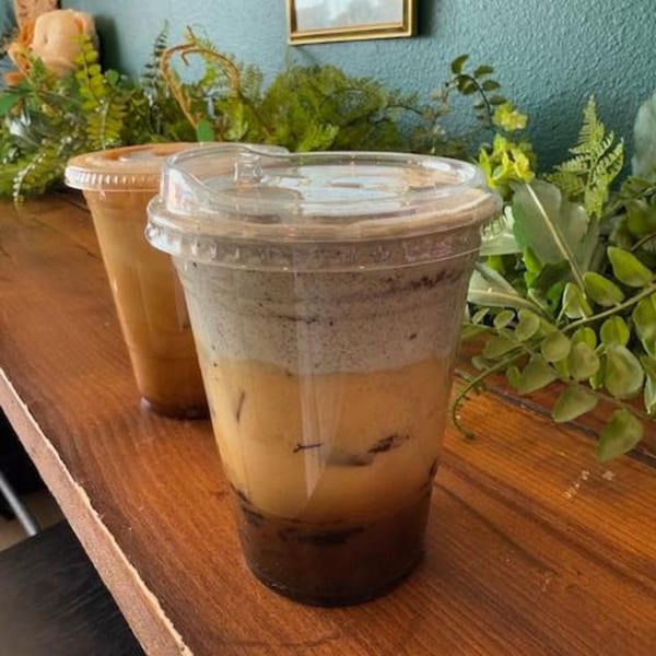 Two iced coffee drinks on a wooden counter, one with layered dark and light cream.