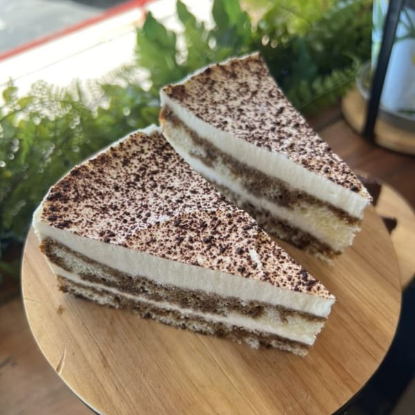 Two slices of tiramisu cake with cocoa powder on a wooden board at KOHI Coffee.