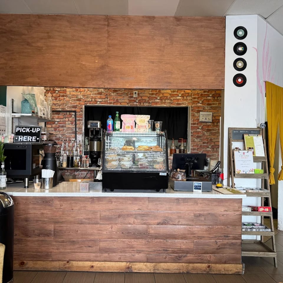 The interior of KOHI Coffee, featuring a wooden counter, brick wall, and a display case with pastries.