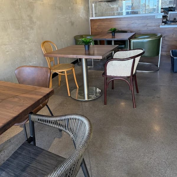 Interior of KOHI Coffee with various tables and chairs, concrete floor, and a wooden paneled wall.
